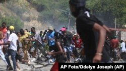 Un grupo de personas huye del gas lacrimógeno disparado por la policía para dispersar a los manifestantes que exigen a la policía y al primer ministro que actúen de inmediato contra las pandillas, en Puerto Príncipe, Haití, el lunes 19 de agosto de 2024. (AP Foto/Odelyn Joseph)
