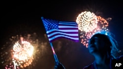 Una mujer observa los fuegos artificiales y sostiene una bandera de los Estados Unidos durante la celebración del 4 de julio.