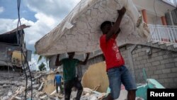 Dos hombres cargan un colchón del sitio de un hotel derrumbado después del terremoto de magnitud 7,2 del sábado, en Les Cayes, Haití, 16 de agosto de 2021.