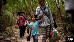 Una mujer camina con sus hijos a través del río Táchira, por las trochas que conectan a Venezuela con Colombia.