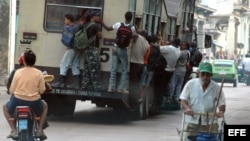 Varias personas viajan colgando de un ómnibus, popularmente conocido como camello