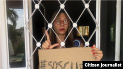 Iliana Hernández, atrapada en su hogar, con un cartel de #SOSCUBA.