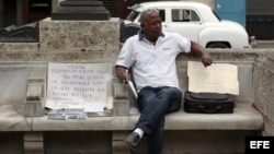 Un hombre, improvisado agente inmobiliario, ofrece varias casas en venta sentado en un parque.