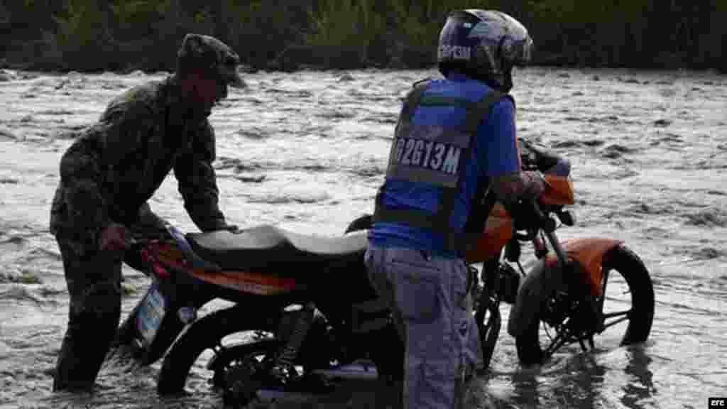 Un soldado colombiano ayuda a un motociclista a cruzar el Río Táchira