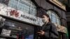 Mujer con mascarilla delando de una tienda de la empresa Huawei en China.